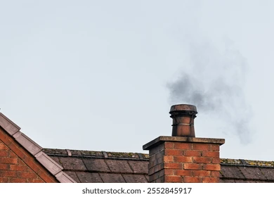 Smoke rising from a brick rooftop chimney