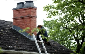 Technician inspecting a brick chimney on a shingle roof with a ladder.